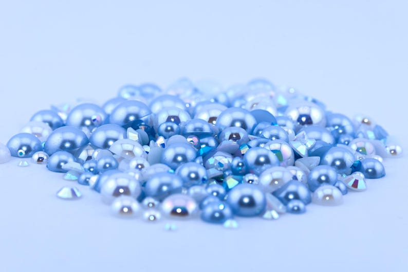 May include: A pile of light blue and white pearl-like beads and rhinestones. The beads are various sizes and shapes.