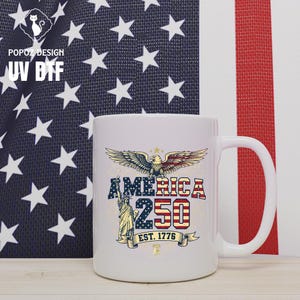 May include: White ceramic mug with a patriotic design featuring an eagle, the Statue of Liberty, and the text "AMERICA 250 EST. 1776". The mug has a large handle and is set against an American flag background.