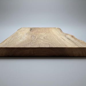 May include: A natural wood cutting board with a live edge. The rectangular board is made of light brown wood with visible grain and a smooth, curved edge. The board is approximately 1 inch thick.