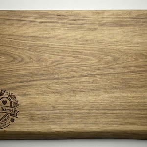 May include: Rectangular wooden cutting board with a light brown finish. The board features a decorative emblem with a crown, hearts, and the text "[Name] & [Name]" and "Seit (Datum)".