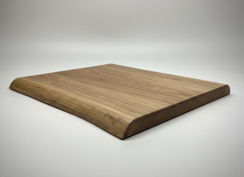 May include: A square, light brown wooden cutting board with a natural edge on one side. The board has a smooth surface and rounded corners. The wood grain is visible, adding to its rustic appeal. This kitchen item is perfect for food preparation.