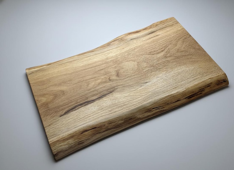 May include: A rectangular wooden cutting board with a natural, live edge. The board is made of light-colored wood with darker grain patterns and measures approximately 18 inches long and 12 inches wide.