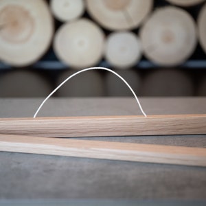 May include: A wooden poster hanger with a white string attached to the top. The hanger is made of natural wood and has a simple design.