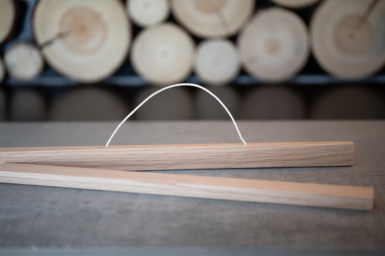 May include: A wooden poster hanger with a white string attached to the top. The hanger is made of natural wood and has a simple design.