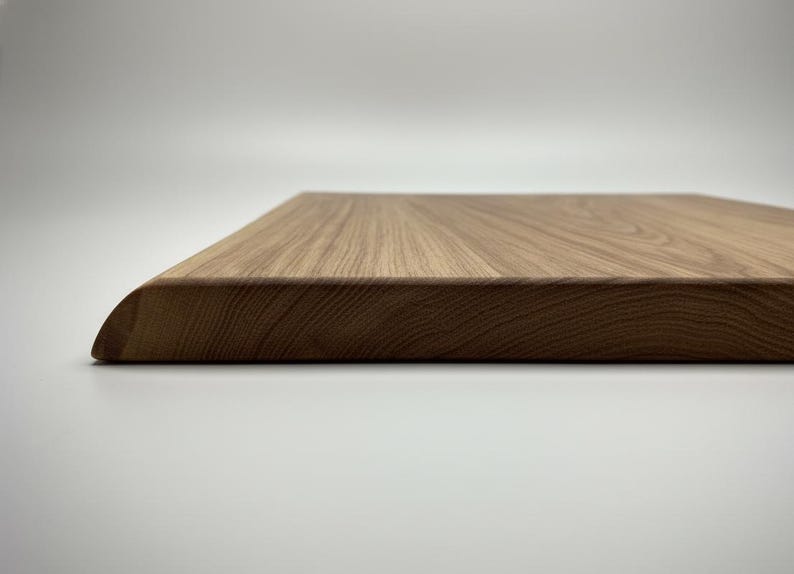 May include: Close-up of a rectangular wooden cutting board with a rounded corner. The board has a natural wood grain pattern and a light brown color. The board is likely used for food preparation.