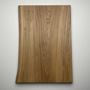 May include: A rectangular wooden cutting board with a natural edge. The board is made of light brown wood with visible grain patterns. The board is approximately 18 inches long and 12 inches wide.