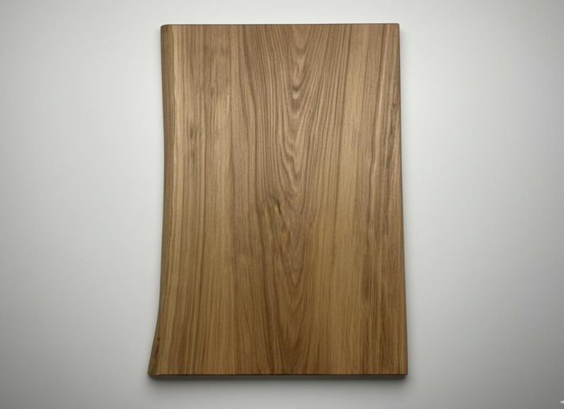 May include: A rectangular wooden cutting board with a natural edge. The board is made of light brown wood with visible grain patterns. The board is approximately 18 inches long and 12 inches wide.