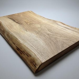May include: A rectangular wooden cutting board with a natural edge. The board is made of light-colored wood with visible grain and a smooth, finished surface. The board is approximately 12 inches long and 8 inches wide.