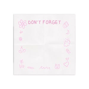 Puede incluir: Un papel blanco doblado con las palabras "DON'T FORGET" en rosa, rodeado de garabatos rosas de una flor, cerezas, un gato y otras pequeñas ilustraciones. El papel está centrado sobre un fondo blanco.