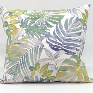 May include: A white cushion with a tropical leaf pattern in shades of green, blue, and yellow.