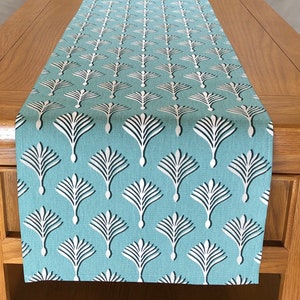 May include: A teal table runner with a white geometric pattern of stylised palm trees.