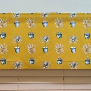 May include: A yellow valance with a repeating pattern of potted plants. The plants have grey pots and green leaves.
