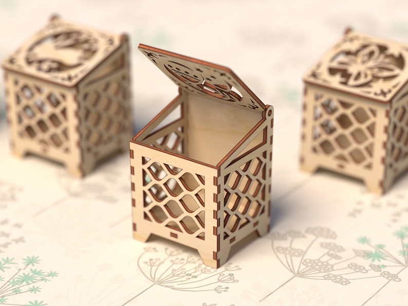 May include: Three wooden boxes with intricate cut-out designs. The box in the center is open, revealing the empty interior. The boxes are made of light brown wood and have a delicate, lacy appearance.