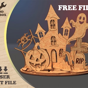 May include: Laser-cut wooden Halloween decoration with a haunted house, pumpkin, ghost, spider, and tombstone. The text "FREE FILE" and "LASER CUT FILE" are visible. The Wood Toolbox logo is in the upper left corner.