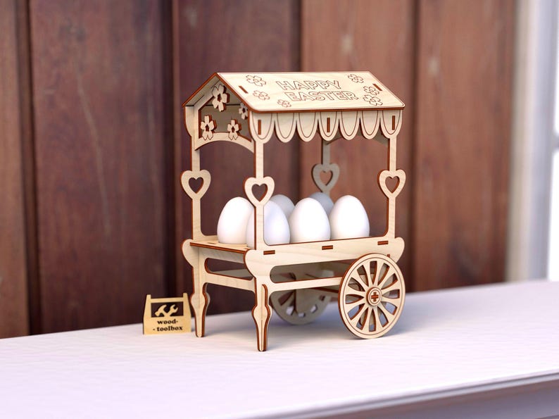 May include: A wooden Easter egg cart with a sign that reads "Happy Easter". The cart has a white background and is decorated with hearts and flowers. It is filled with six white eggs.