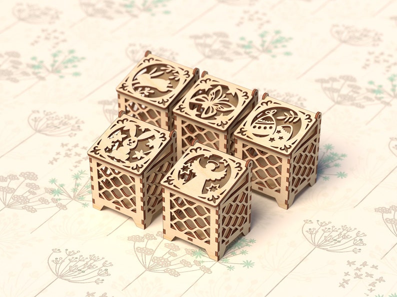 May include: Five wooden boxes with intricate laser cut designs. Each box features a different design, including a bunny, a flower, an angel, and an Easter egg. The boxes are all made of natural wood and have a light brown color.
