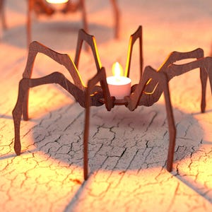 Peut inclure: Bougeoirs en forme d'araign&eacute;e en bois, chacun avec une bougie blanche allum&eacute;e. Les araign&eacute;es marron ont de longues pattes et sont pos&eacute;es sur une surface textur&eacute;e. La lueur chaleureuse des bougies cr&eacute;e une ambiance chaleureuse, id&eacute;ale pour Halloween.