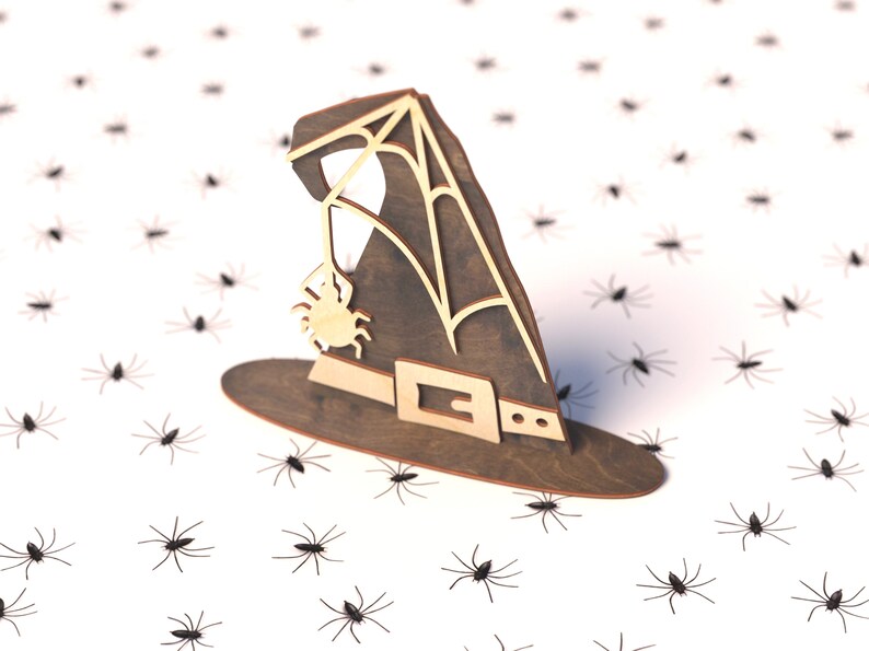 May include: A wooden witch's hat with a spider web design and a spider hanging from the web. The hat is sitting on a white surface with many black spiders scattered around it.