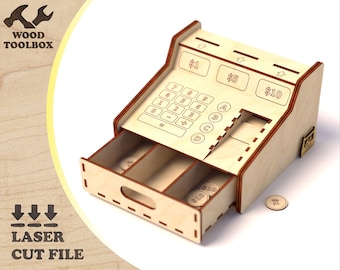 May include: A wooden cash register with a drawer that is open, revealing three compartments. The cash register has a keypad with numbers and symbols, and a display that shows the amounts $1, $5, and $10. There are wooden coins in the drawer.