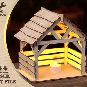 Könnte beinhalten: Eine lasergeschnittene Krippe aus Holz mit einem Satteldach und Lattenseiten. Im Inneren befindet sich eine kleine Kerze, die die Struktur beleuchtet. Der Text "WOOD TOOLBOX" und "LASER CUT FILE" sind sichtbar.