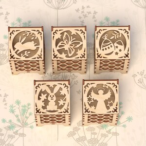 May include: Set of six wooden boxes with intricate laser-cut designs. Each box features a different Easter-themed image, including a bunny, butterfly, eggs, a chick, and an angel.