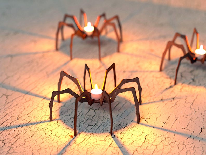 Peut inclure: Trois bougeoirs en forme d'araign&eacute;e en m&eacute;tal marron avec des bougies blanches allum&eacute;es. Les bougeoirs sont sur une surface textur&eacute;e blanc cass&eacute;, projetant des ombres. Les flammes des bougies brillent.