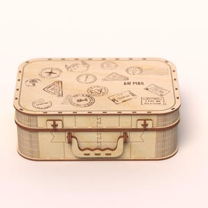 Puede incluir: Una maleta de madera clara con asa y cierres. La parte superior de la maleta est&aacute; decorada con varios sellos y las palabras "AIR MAIL". La maleta rectangular parece estar hecha de madera en capas.