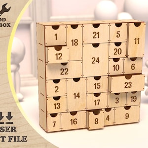 Könnte beinhalten: Adventskalender aus Holz mit 24 nummerierten Schubladen. Der Kalender ist aus lasergeschnittenem Holz gefertigt und trägt die Aufschrift "WOOD TOOLBOX" und "LASER CUT FILE". Eine Schublade ist geöffnet.