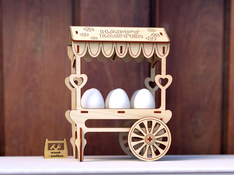 May include: Wooden Easter egg stand shaped like a cart with a sign that reads "Happy Easter". The cart has a white canopy and three white eggs inside.