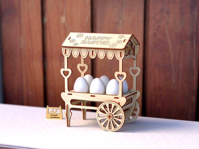 May include: A wooden Easter egg cart with a sign that reads "Happy Easter". The cart has four wheels and is decorated with hearts. It is holding five white eggs.