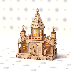 May include: A wooden model of a fairytale castle with a star on top, lit with warm white lights. The castle has a porch with a small figure standing in the doorway.