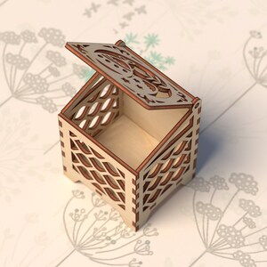 May include: A small wooden box with a decorative, open lid. The box is made of light wood with a brown stain and has a geometric pattern cut into the sides. The box is sitting on a white background.