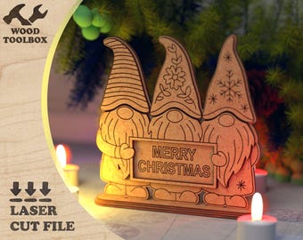 May include: Wooden Christmas gnome decoration with the text "MERRY CHRISTMAS". The gnomes have long hats and beards. The image also includes the text "WOOD TOOLBOX" and "LASER CUT FILE".