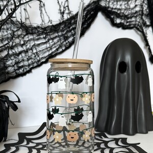 May include: A clear glass reusable water bottle with a bamboo lid and a straw. The bottle has a Halloween themed design with ghosts, bats, pumpkins, and flowers.