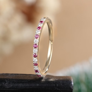 May include: A delicate gold band ring with a row of small red and white gemstones.