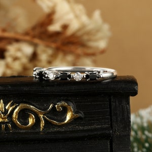 May include: A delicate silver band ring with alternating black and white oval-shaped gemstones. The ring is set on a black surface.