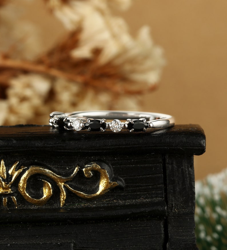 May include: A delicate silver band ring with alternating black and white oval-shaped gemstones. The ring is set on a black surface.