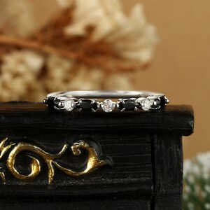 May include: A delicate silver band ring with alternating black and white oval-shaped stones.