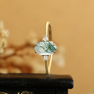 Pu&ograve; includere: Un anello d'oro con una pietra preziosa in agata muschiata verde e bianca e due piccoli diamanti. L'anello &egrave; su una superficie nera.