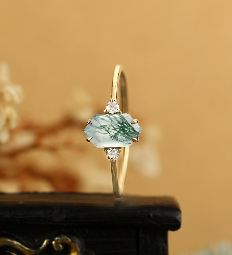 Pu&ograve; includere: Un anello d'oro con una pietra preziosa in agata muschiata verde e bianca e due piccoli diamanti. L'anello &egrave; su una superficie nera.