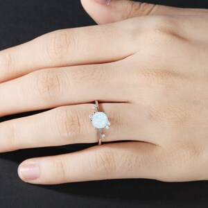 May include: A silver ring featuring a white opal gemstone surrounded by smaller white gemstones.