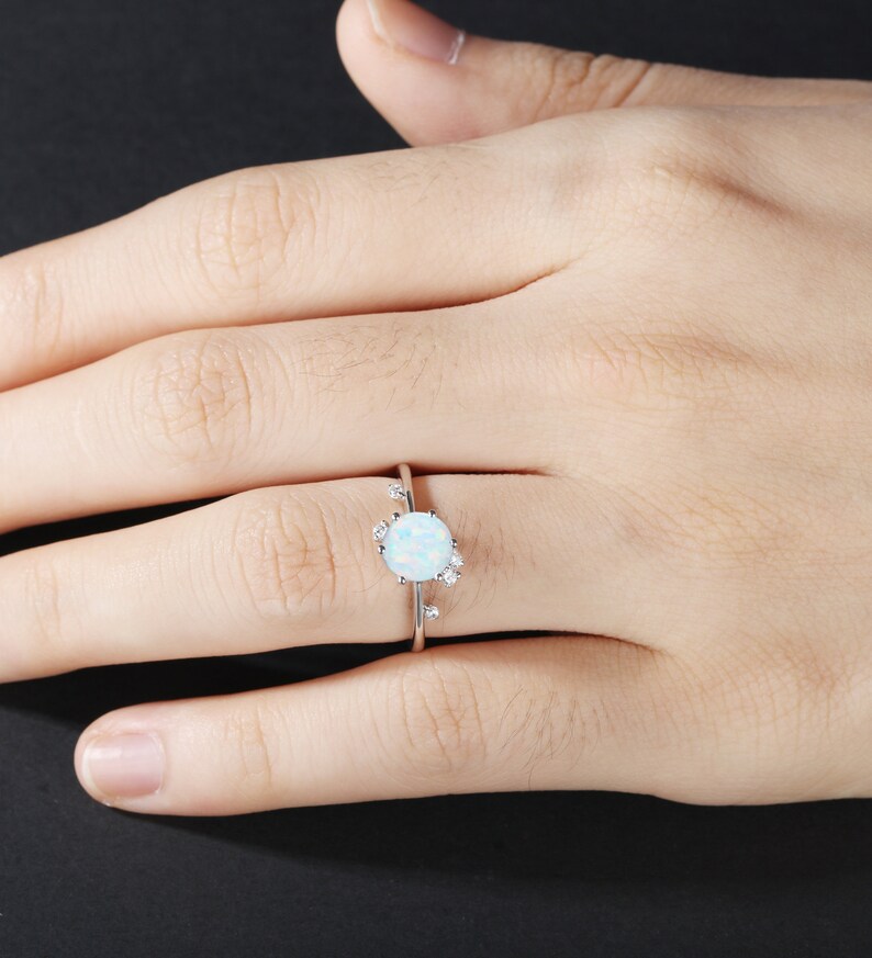 May include: A silver ring featuring a white opal gemstone surrounded by smaller white gemstones.