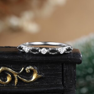 May include: A delicate silver band ring with a row of black onyx stones and small round diamonds.