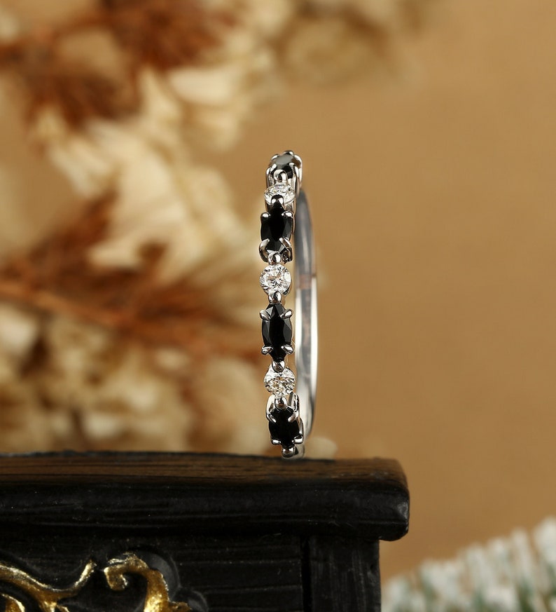 May include: A delicate silver band ring with alternating black and white oval-shaped gemstones.
