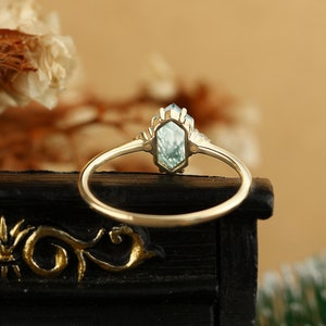 Pu&ograve; includere: Un anello d'oro con una pietra preziosa blu chiaro in una montatura esagonale. L'anello &egrave; incastonato con pietre preziose pi&ugrave; piccole su entrambi i lati della pietra principale.
