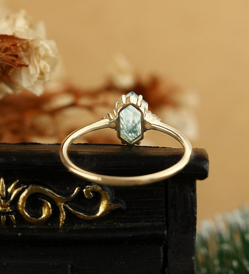 Pu&ograve; includere: Un anello d'oro con una pietra preziosa blu chiaro in una montatura esagonale. L'anello &egrave; incastonato con pietre preziose pi&ugrave; piccole su entrambi i lati della pietra principale.