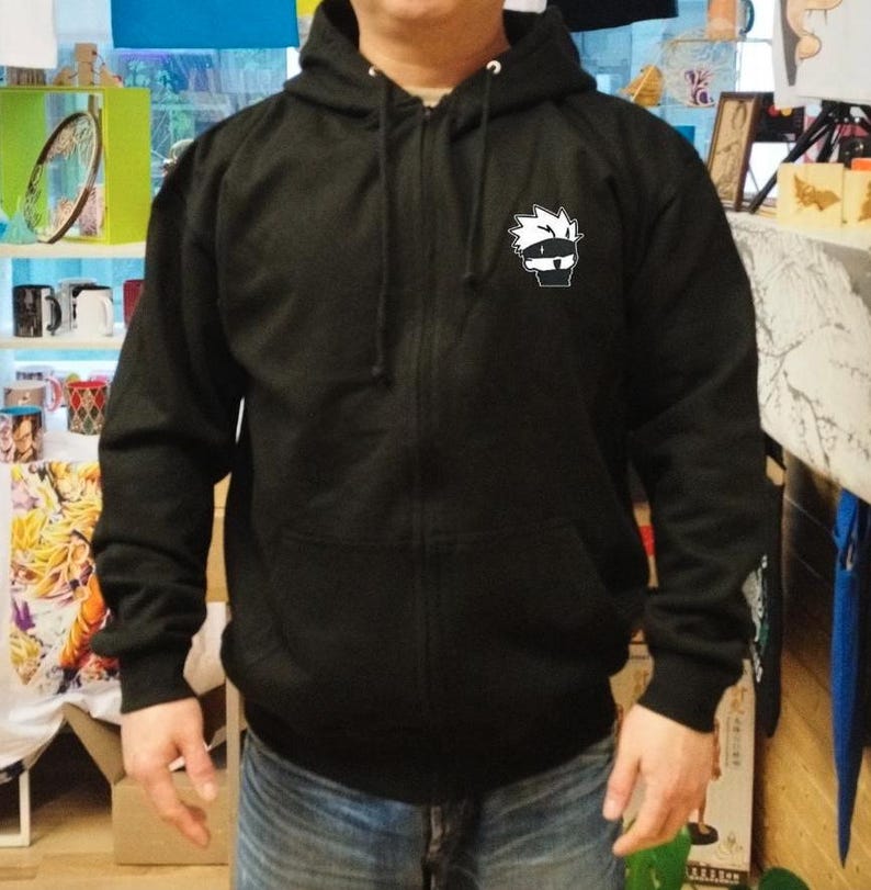 May include: Black zippered hoodie with a white cartoon character on the front. The character has spiky hair and is wearing a headband.