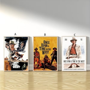 May include: Three framed film posters for "Once Upon a Time in the West" are shown. The posters feature images of cowboys and the film's title. The posters are arranged in a row against a light-coloured wall.