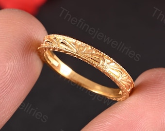 May include: A gold wedding band with a delicate, intricate floral design. The band is thin and has a polished finish.
