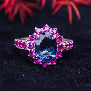 May include: A silver ring with a large blue oval gemstone surrounded by a halo of smaller pink gemstones.